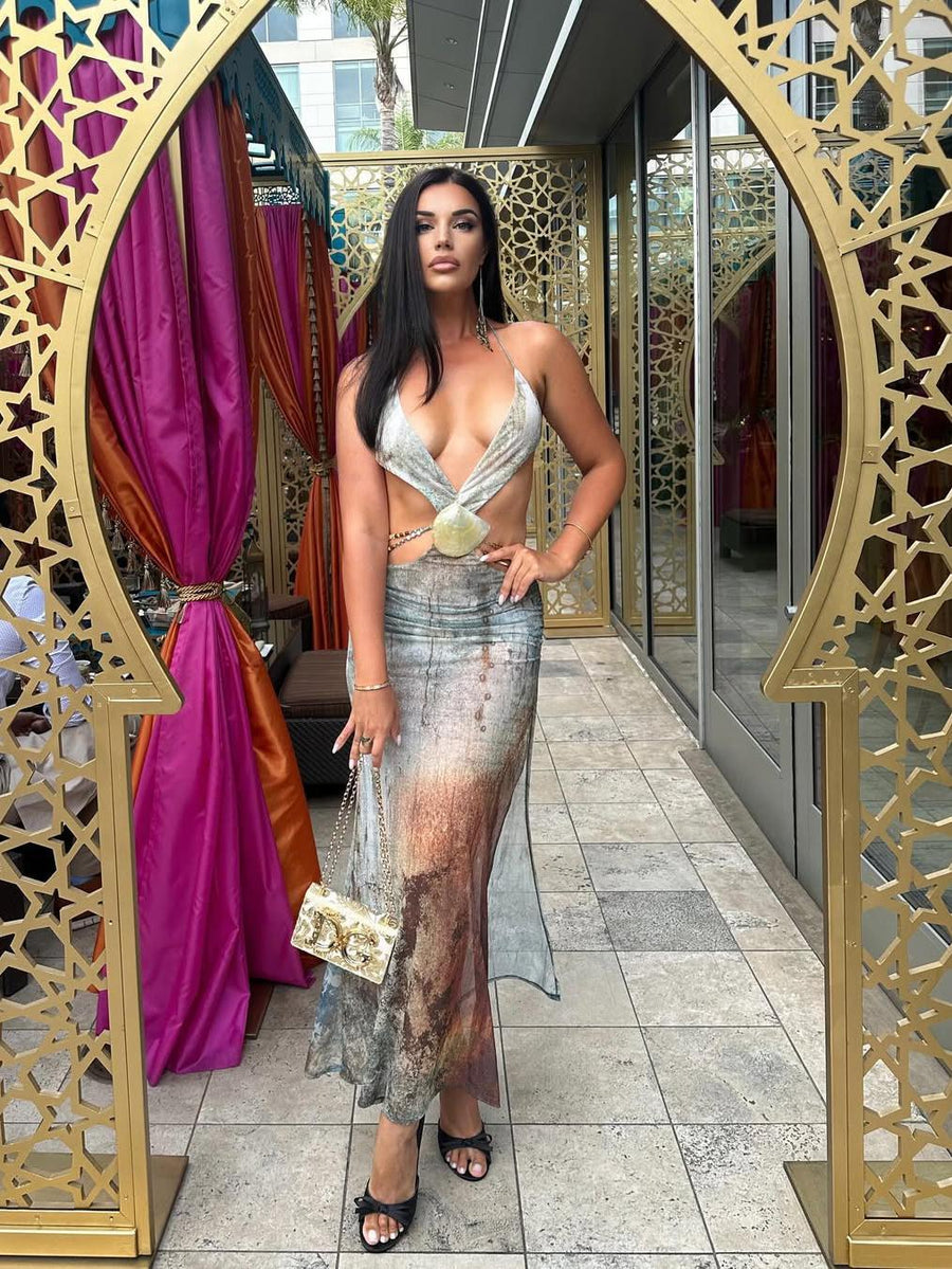 Model in silver-to-bronze tie-dye dress with beaded straps, deep V-neck and shell cutout, standing beside gold lattice arches.