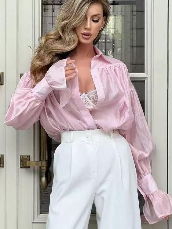 Soft pink oversized shirt with wide ruffle cuffs, tucked into white high-waisted trousers; lace top peeks at the chest.