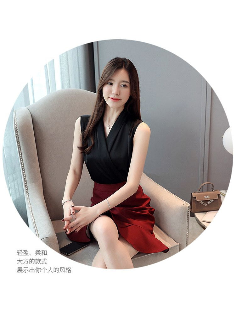 Model seated in a beige armchair wearing a black satin sleeveless wrap top and a red skirt.
