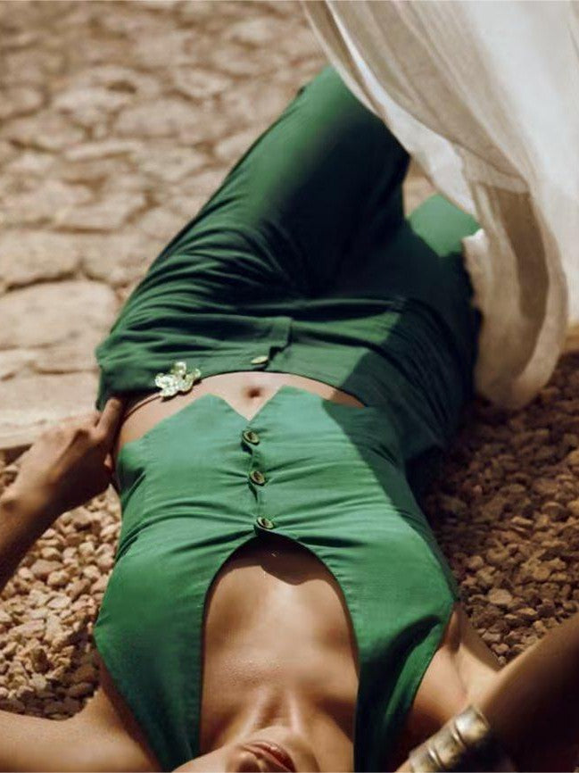 Emerald green halter-neck vest with front buttons and wide-leg pants; model lying on rocky ground beside white fabric.