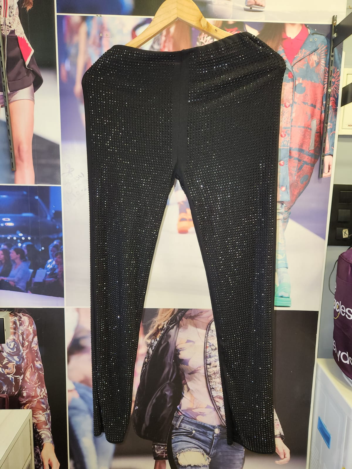 Black rhinestone pants on a wooden hanger, full-length with all-over sparkle, set against a fashion collage backdrop.
