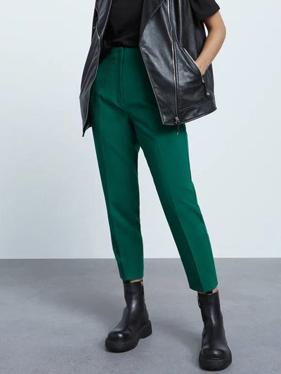 Green high-waisted ankle-length pants paired with a black top, black leather biker jacket, and chunky black boots.