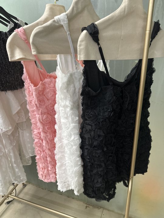 Rosette-textured bodycon mini dresses in pink, white, and black with thin straps hanging on a metal clothing rack.