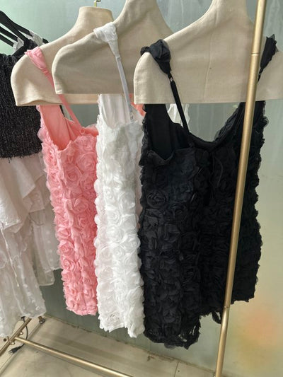 Rosette-textured bodycon mini dresses in pink, white, and black with thin straps hanging on a metal clothing rack.