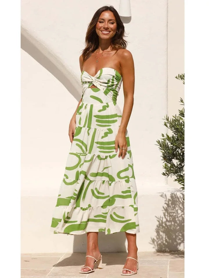 Smiling woman in a strapless white dress with green floral print, bow knot at the bust, tiered midi skirt, white sandals.