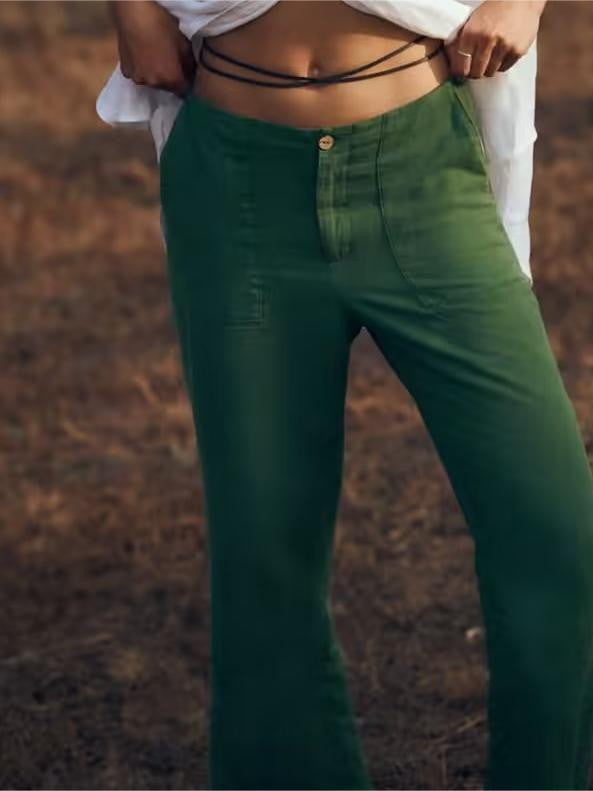 Emerald-green high-waisted wide-leg pants with a wooden button, shown with a white cropped top and black cord belt.