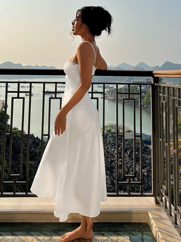 Side profile of a woman in a white satin spaghetti-strap dress with lace detailing, tea-length, on balcony with a view.