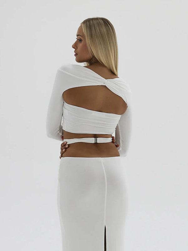 Model wearing white two-piece coord set: cropped long-sleeve top with back cut-out and high-waisted skirt with a slit.