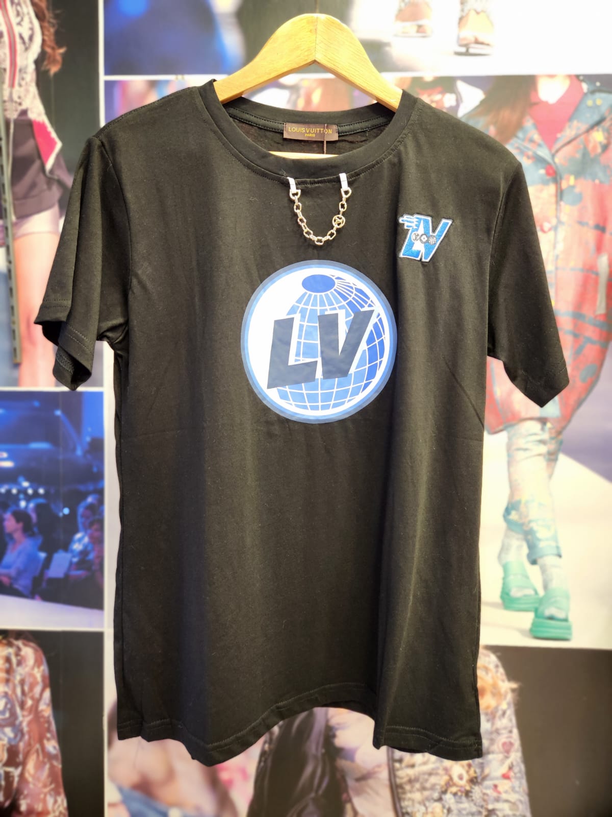 Black cotton-lycra T-shirt on a hanger with a large blue LV globe logo on front and a small LV patch; silver chain.