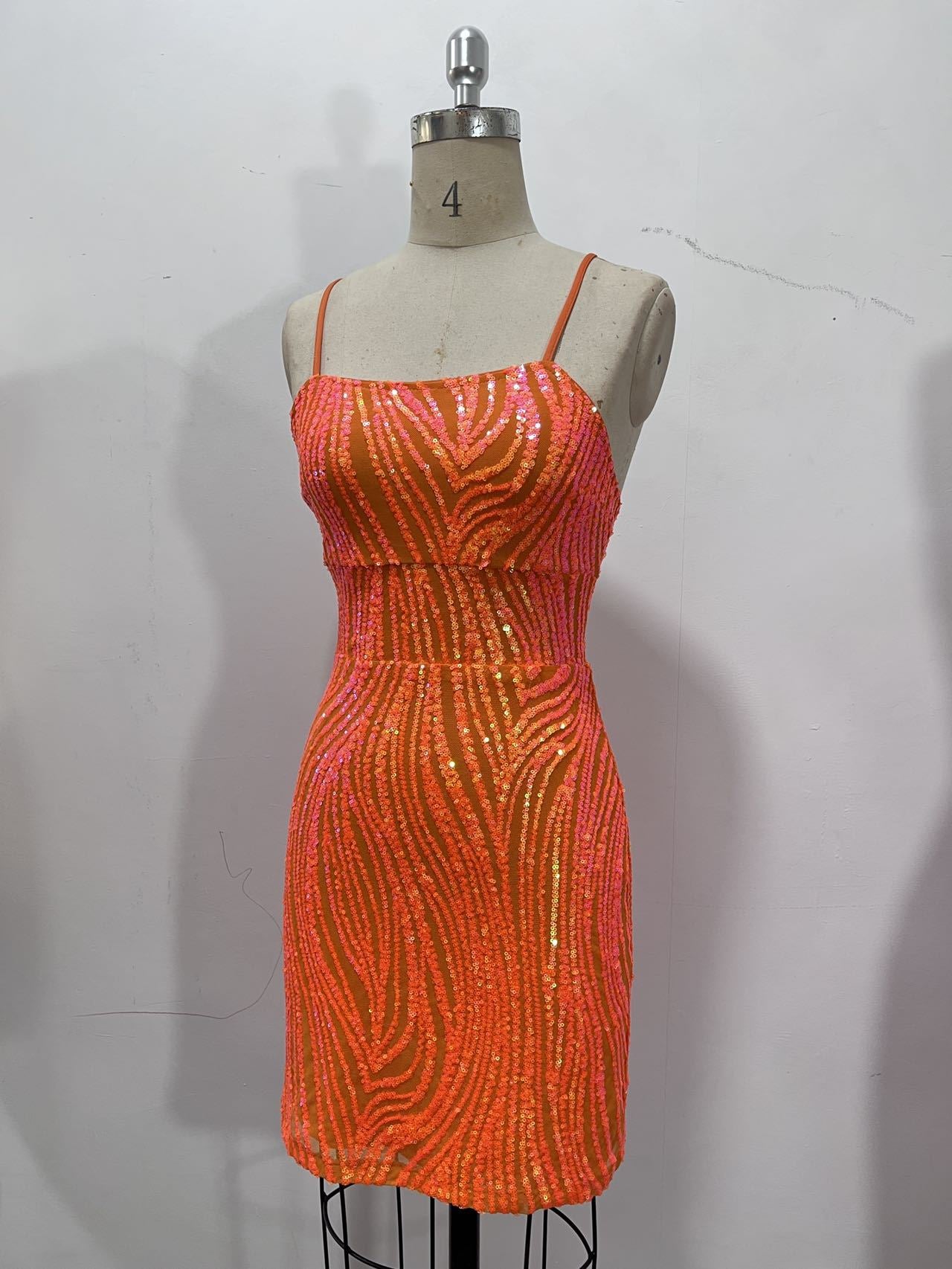 Coral-orange sequin mini dress with thin straps and glittery wavy stripe pattern on a dress form.