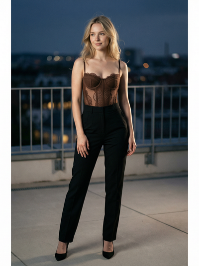 Woman on a rooftop at dusk wearing a brown sheer lace corset bustier top with black high-waisted trousers and heels.