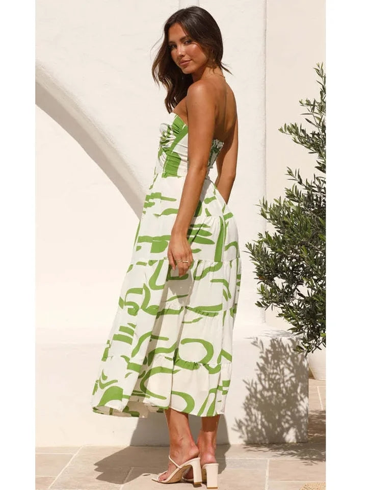 Model in strapless green and white floral print bandeau midi dress with bow knot, standing beside a white wall and plant