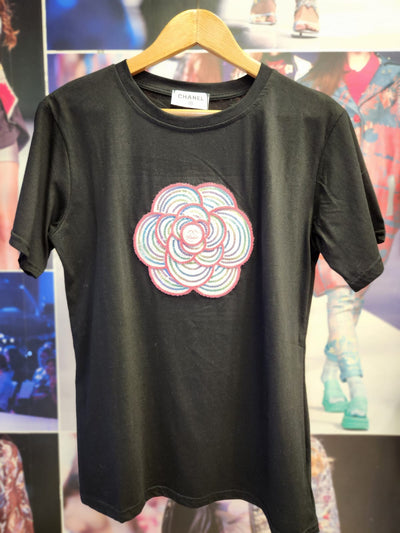 Black cotton Lycra T-shirt on hanger with large multicolor circular flower embroidery on chest; Chanel label at neck.