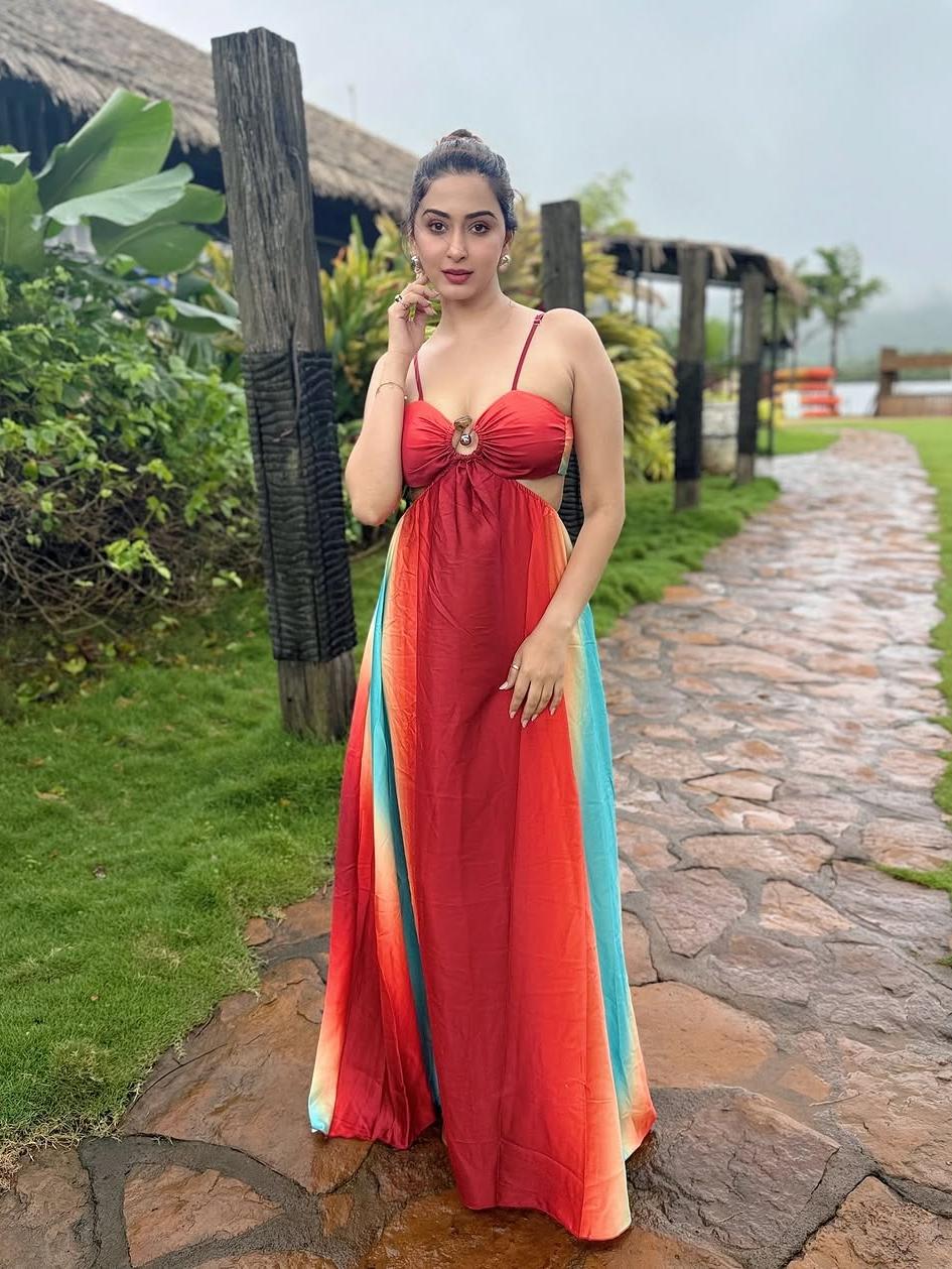 Woman in red-orange tie-dye maxi dress with a front ring cutout and turquoise side panels, standing on a stone path.