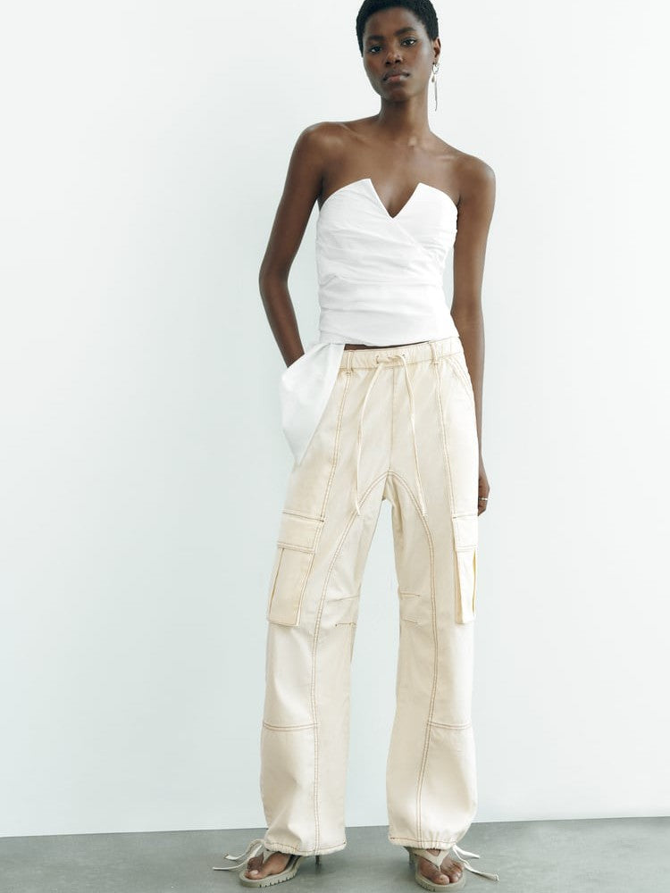 White asymmetric V-neck strapless tube top with light beige cargo pants; model standing against a pale wall.
