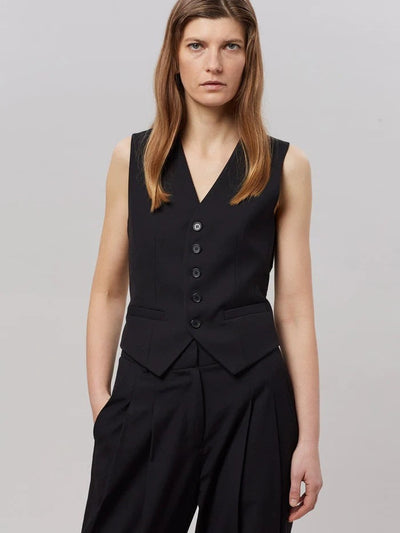 Black sleeveless waistcoat with five buttons over matching wide-leg pleated pants; hands in pockets.