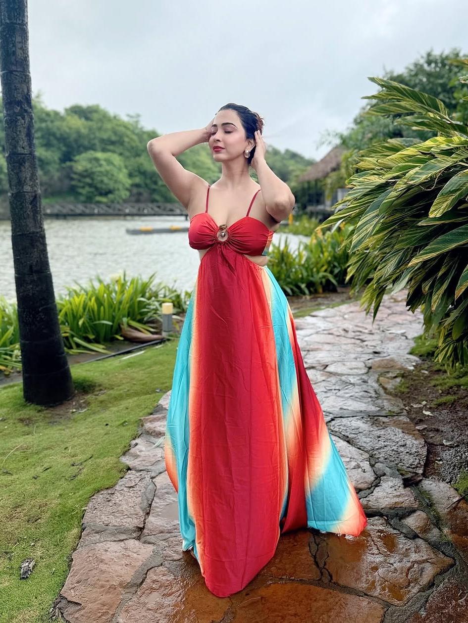 Woman in gradient tie-dye cutout maxi dress, red ruched bodice and thin straps, turquoise and orange panels by a lake.