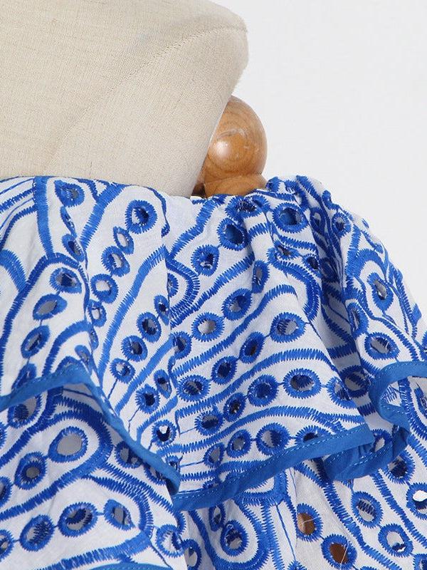 Off-shoulder white cotton dress with blue embroidered circular motifs and a ruffled neckline.