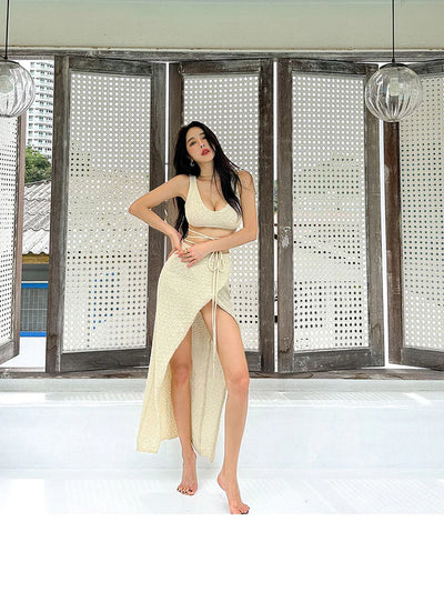 Cream crochet bikini top with matching high-slit wrap skirt, model barefoot in a sunlit patio with lattice panels.