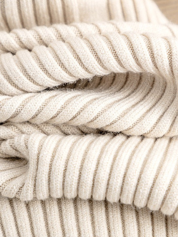 Close-up of cream knitted fabric with thick, evenly spaced ribbing and folded layers.