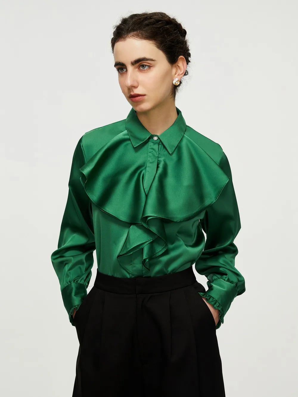 Emerald satin blouse with oversized ruffle placket, pointed collar, and long sleeves, paired with black trousers.