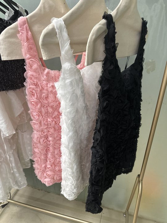 Pink, white, and black rosette-textured bodycon mini dresses on a rack with 3D rose appliques and thin straps.