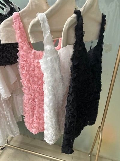 Pink, white, and black rosette-textured bodycon mini dresses on a rack with 3D rose appliques and thin straps.