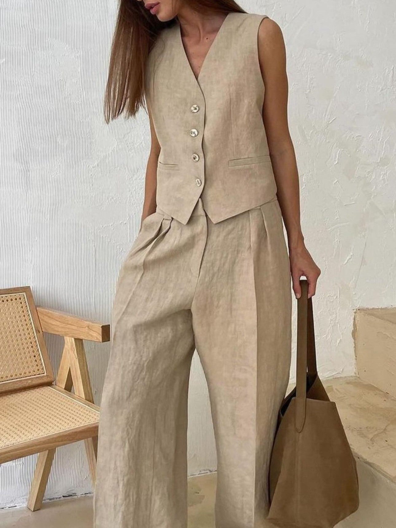 Beige sleeveless waistcoat vest with five buttons paired with matching wide-leg pleated pants; model holds a brown tote.