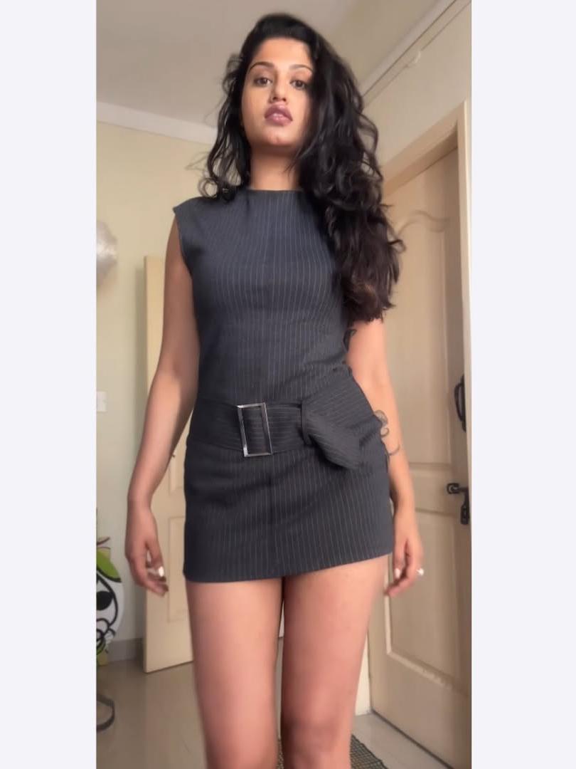 Dark pinstripe sleeveless mini dress with a wide black belt and attached waist pouch, woman standing in doorway.