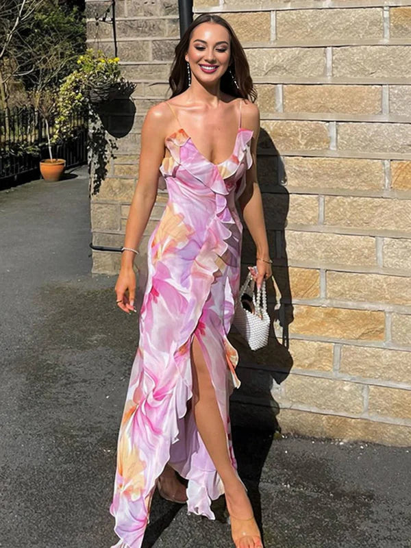 Woman in pastel floral print maxi dress with thin straps, ruffled V-neck, cascading frills, and a high slit, outdoors.