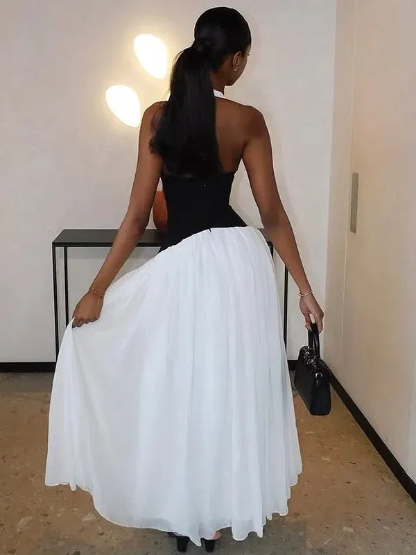Back view of a woman wearing a black halter corset top and a white full maxi skirt, holding a small black purse.