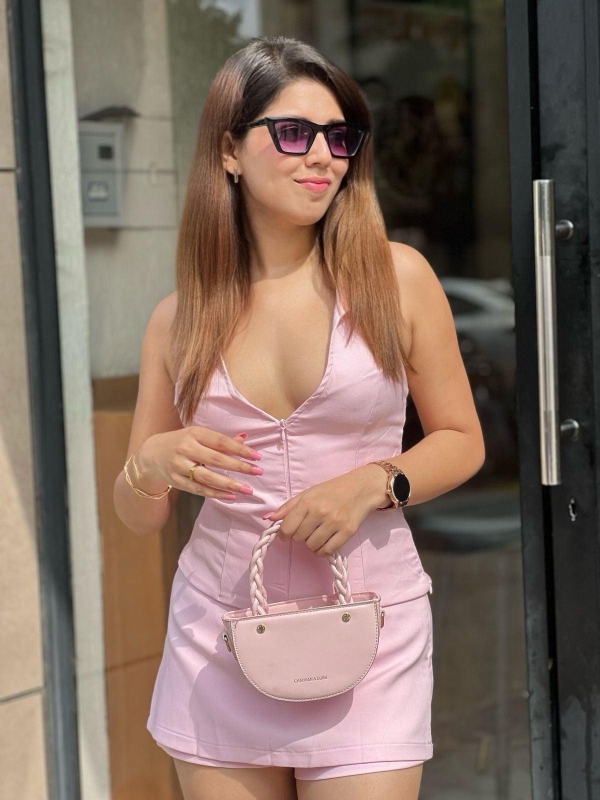 Model wearing pink halterneck waistcoat with a matching skort, holding a pale pink braided handbag outdoors.