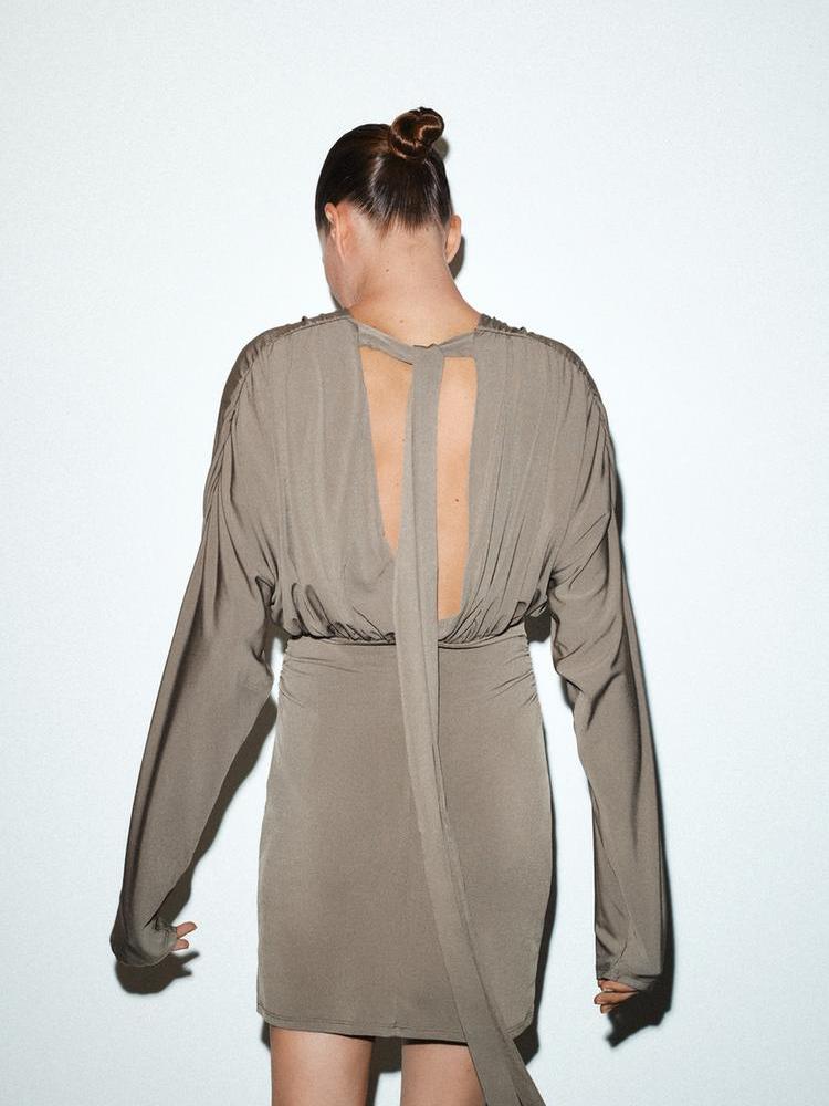 Taupe long-sleeve mini dress seen from the back, with a deep open back and a long sash tying at the neck, cinched waist.