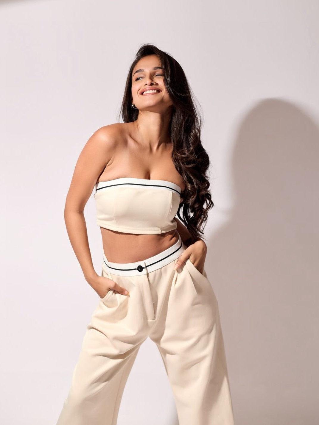 Cream bandeau tube top and matching wide-leg pants with black striped trim; model smiles, hands in pockets.