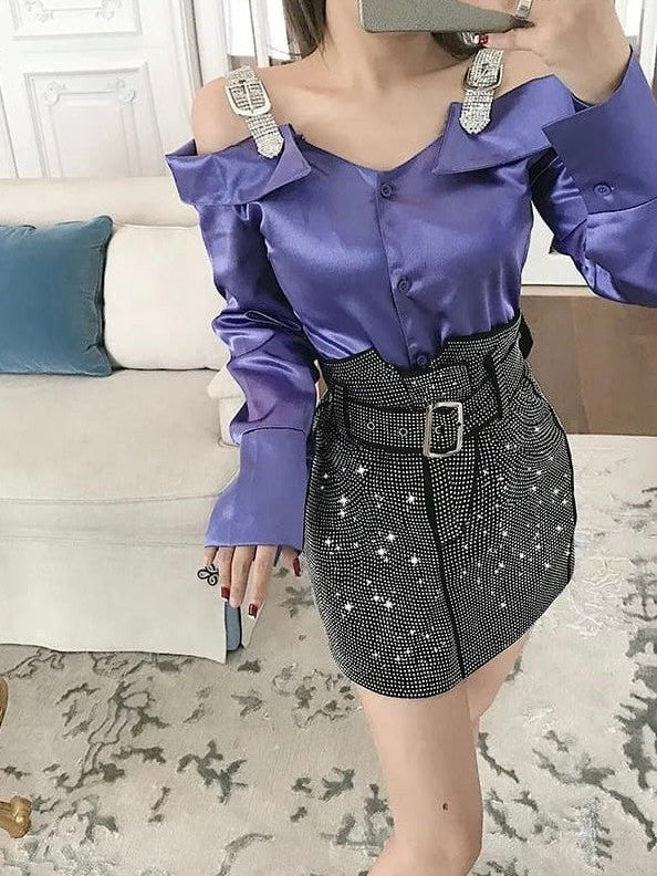 Purple satin off-shoulder blouse with rhinestone shoulder straps; black sequin mini skirt with wide belt.