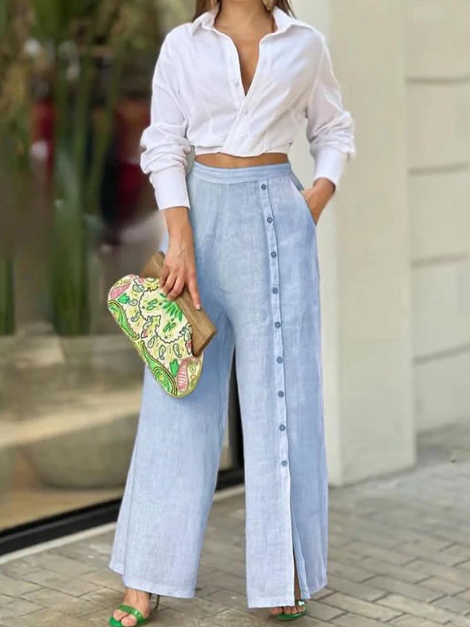 White cropped button-down shirt knotted at waist with light-blue linen wide-leg pants; holds a colorful patterned clutch.