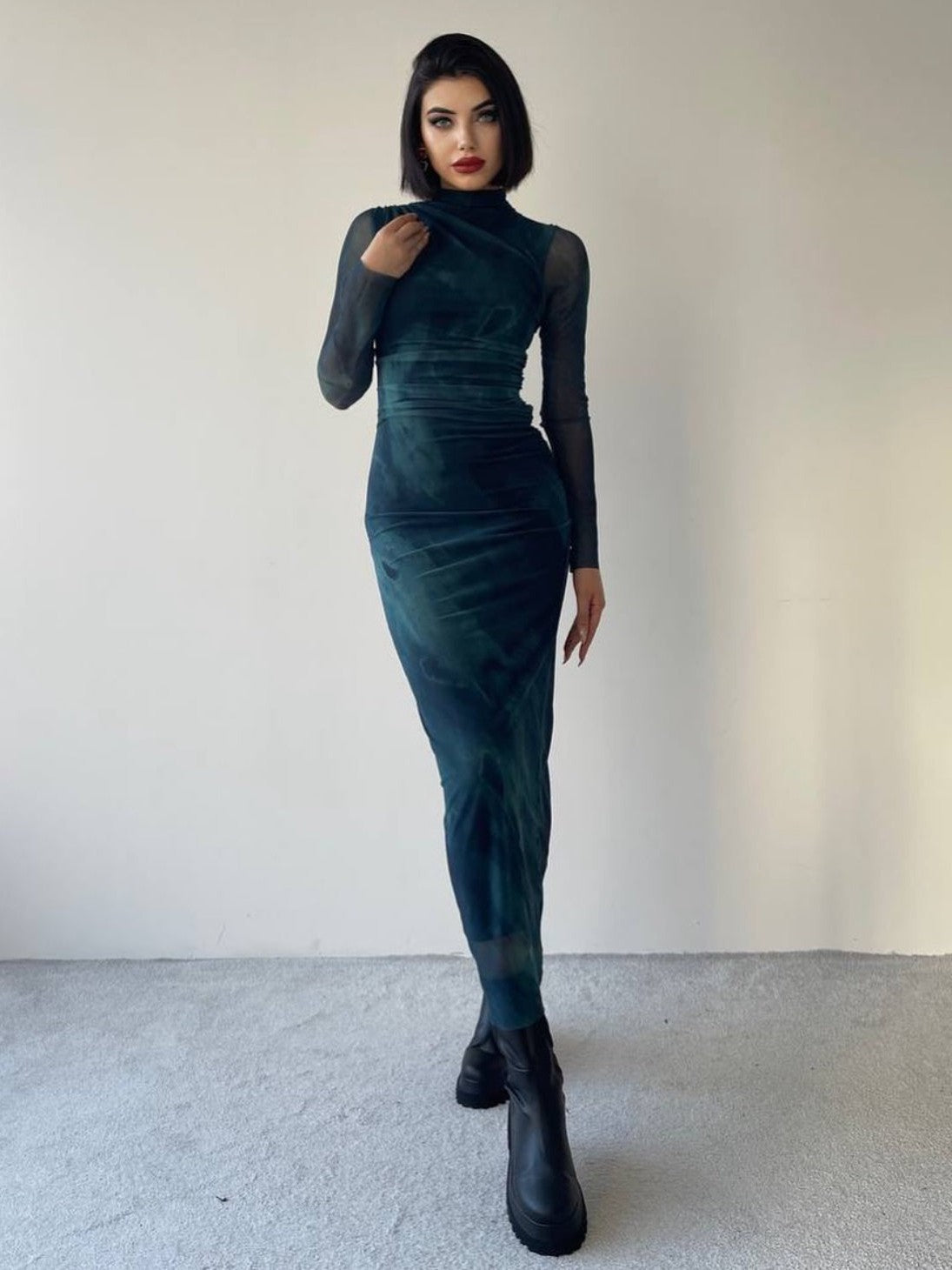 Teal tie-dye high-neck mesh dress with sheer long sleeves, bodycon fit, worn with black chunky boots.