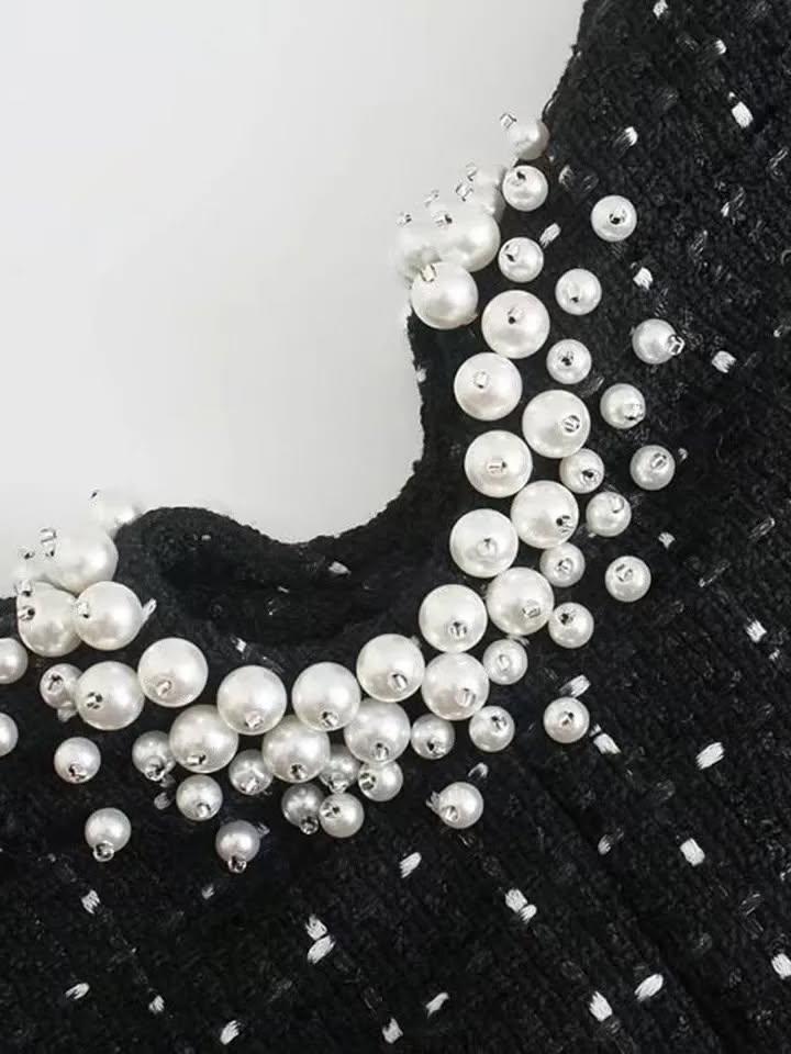 Black tweed fabric with a curved cutout neckline adorned by a cluster of white faux pearls.