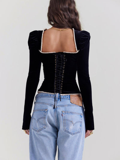 Back view of black velvet lace-up corset top with white rope trim and gold eyelets, worn with light-wash jeans.