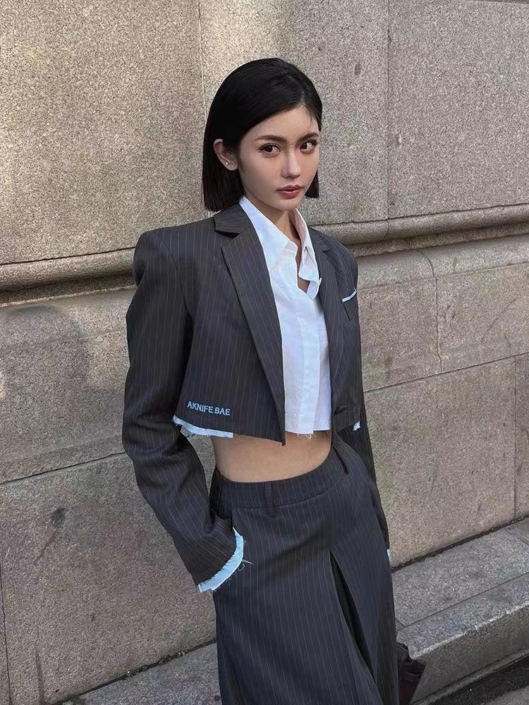 Woman in a dark pinstripe cropped blazer over a white shirt and matching pinstripe wide-leg pants with light-blue frayed cuffs and front slit.