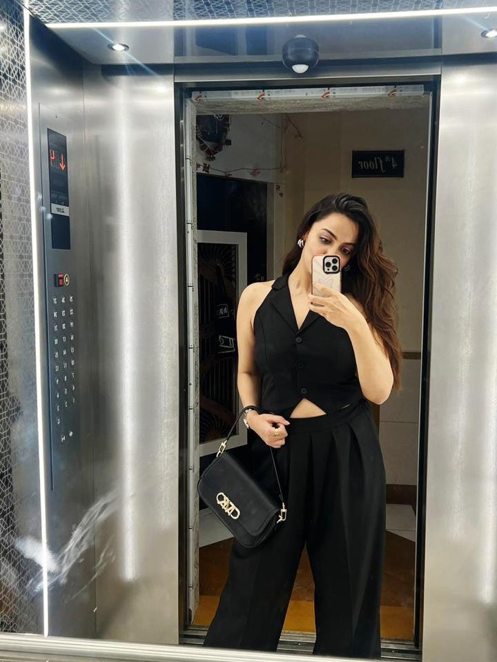Black crop waistcoat with V-neck and midriff cut-out, paired with wide-leg pants; pose with handbag in elevator.