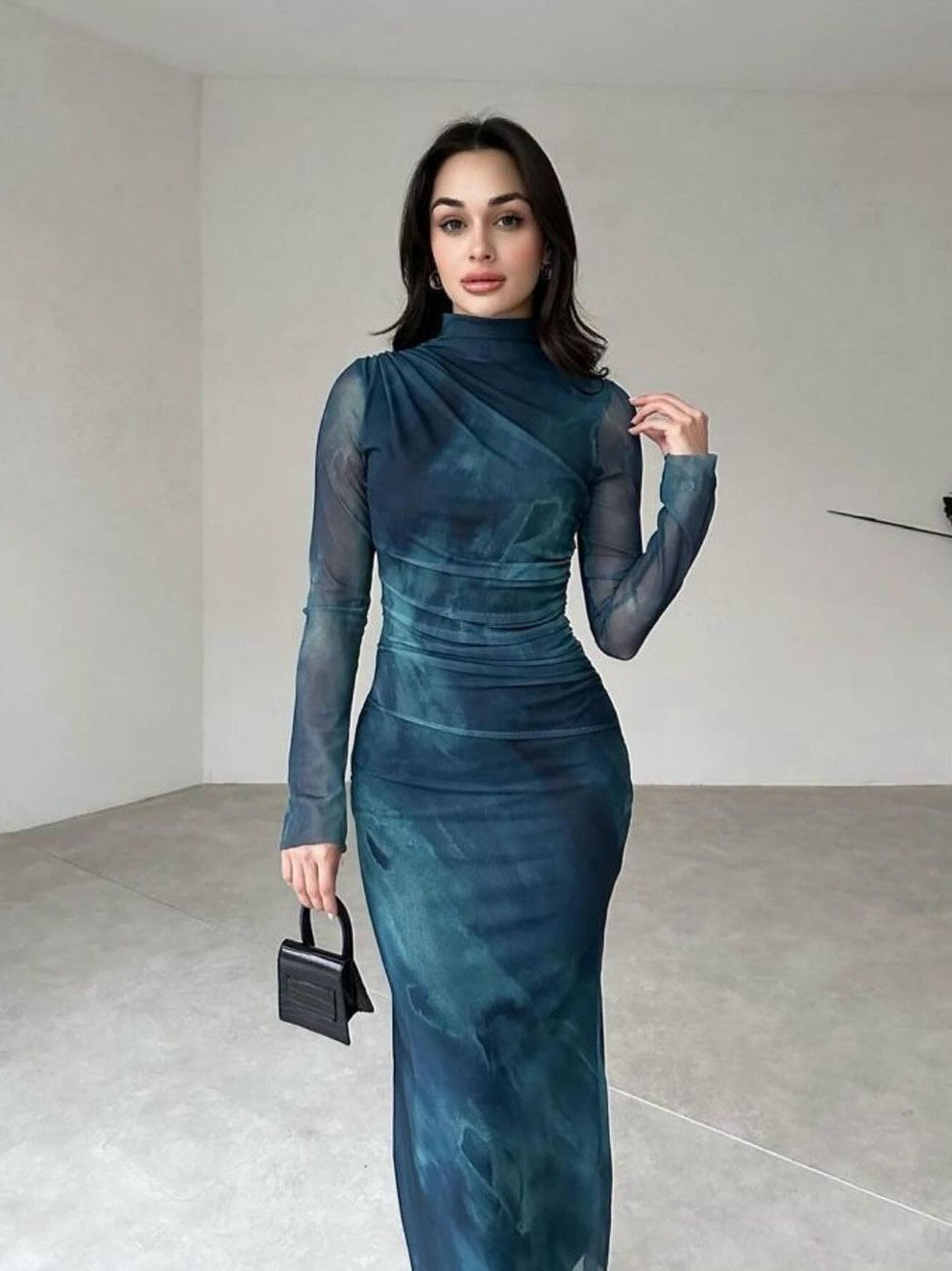 Teal tie-dye mesh maxi dress with high neck and sheer long sleeves, ruched waist, model holding a small black handbag.