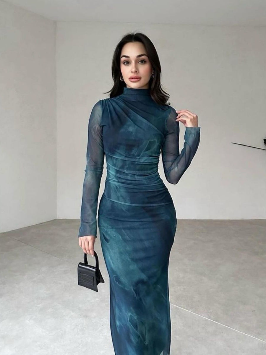Teal tie-dye mesh maxi dress with high neck and sheer long sleeves, ruched waist, model holding a small black handbag.