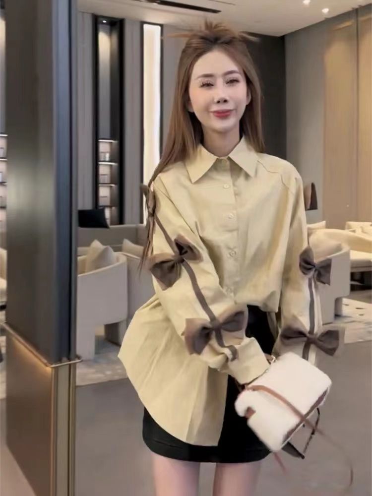 Beige oversized shirt with dark brown bow appliques along sleeves; model with black mini skirt and white fluffy clutch.