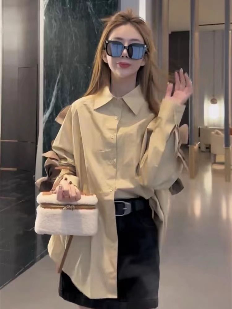 Beige oversized button-down with bow-sleeve detail, black mini skirt with belt, white fluffy handbag, square sunglasses.