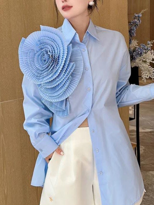 Light blue long-sleeve button-down shirt with a large circular pleated blue flower patch on the left shoulder.