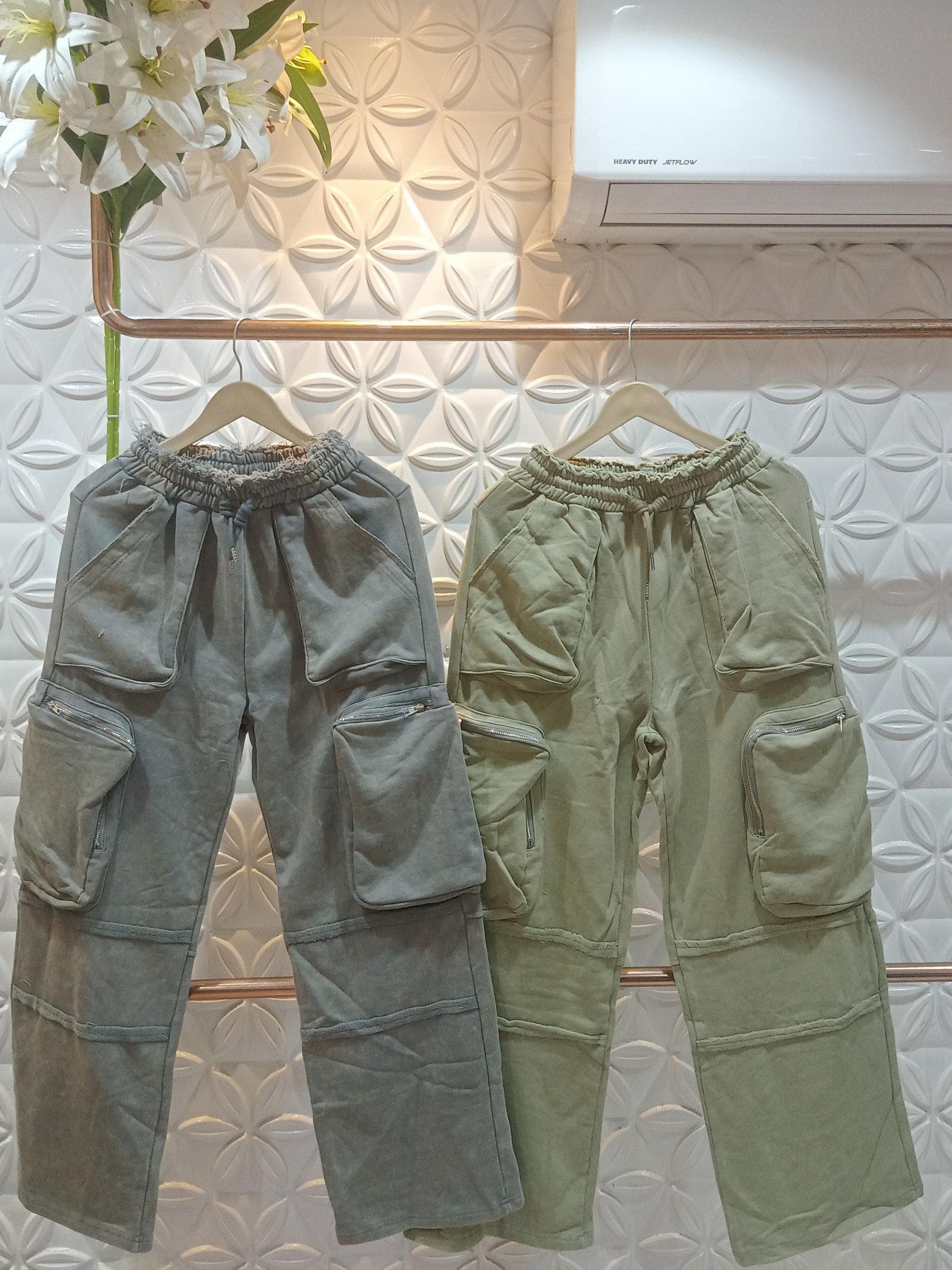 Gray-blue and olive cargo wide-leg pants with oversized patch pockets and zippered side pockets, on wooden hangers.