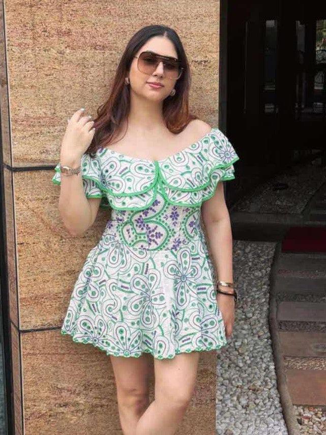 Off-shoulder white cotton dress with green and purple embroidery and ruffled green trim, short flared hem; woman wearing sunglasses.