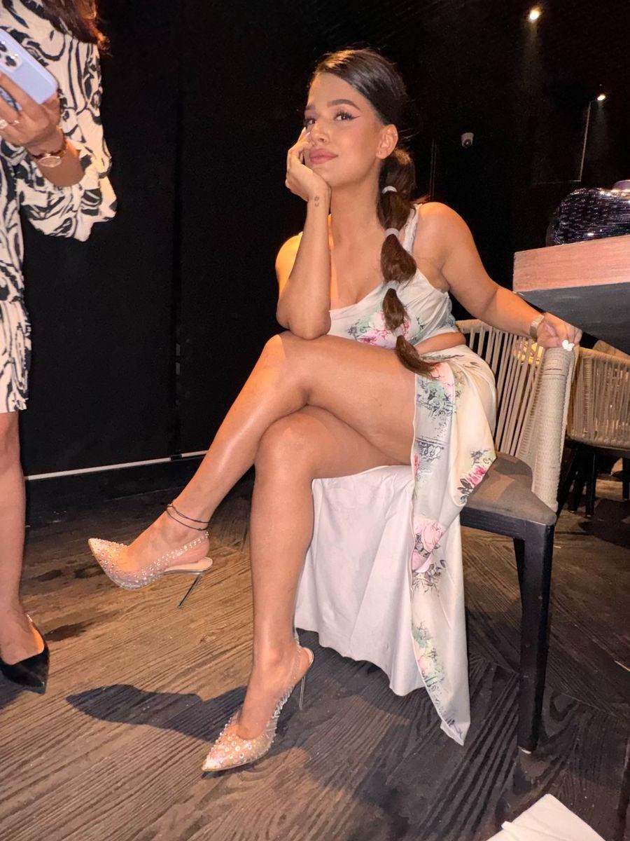 Model wearing floral-print pleated coord set with high-slit skirt, braided ponytail, crystal-embellished nude heels.