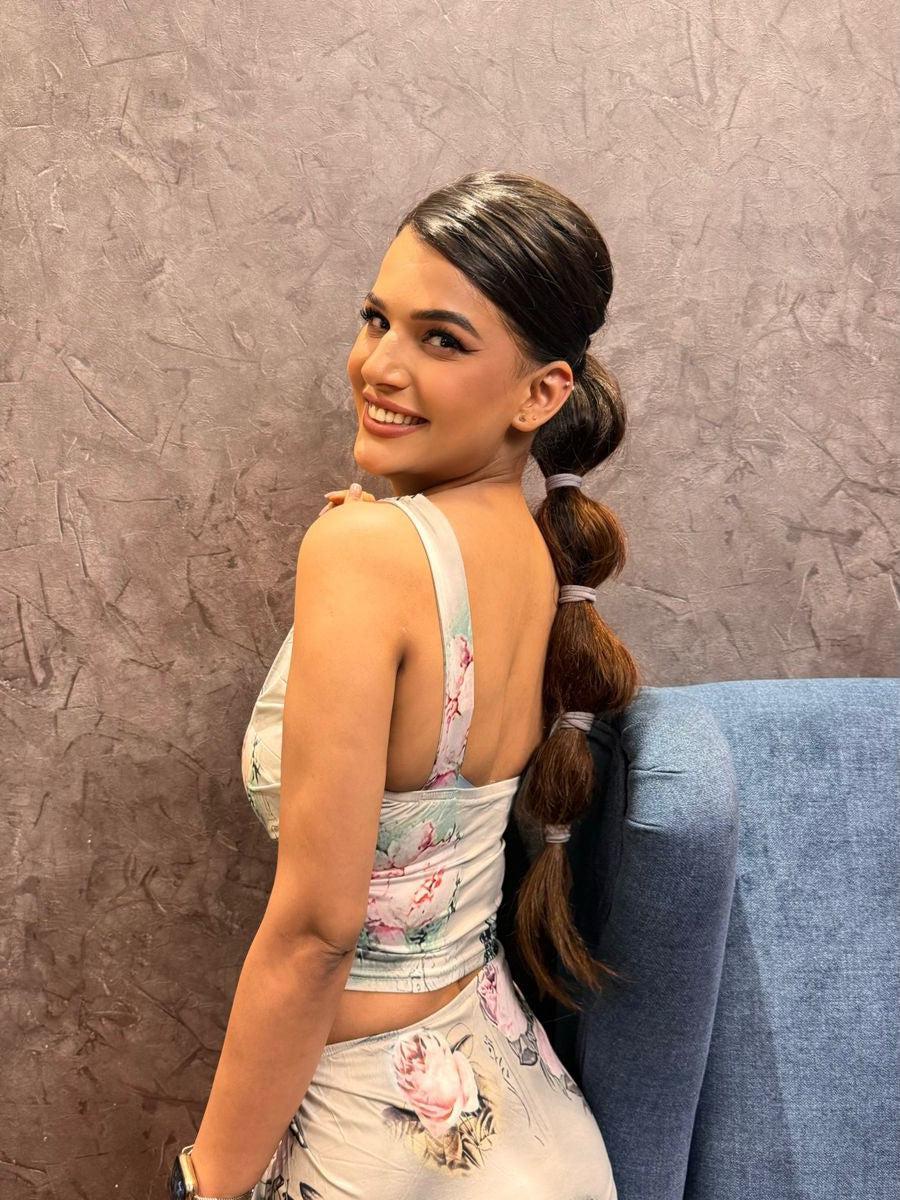 Side view of a woman in pastel floral crop top and high-slit pleated skirt, with long braided ponytail.